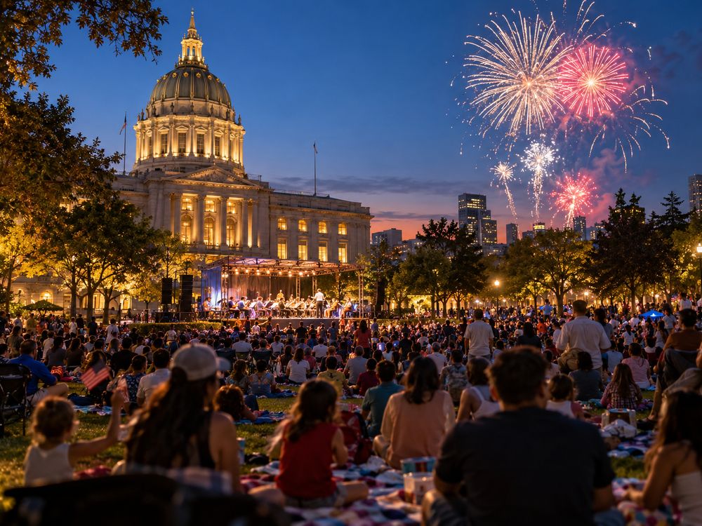 Families on picnic blankets watching a band and fireworks in front of a domed city hall at dusk.