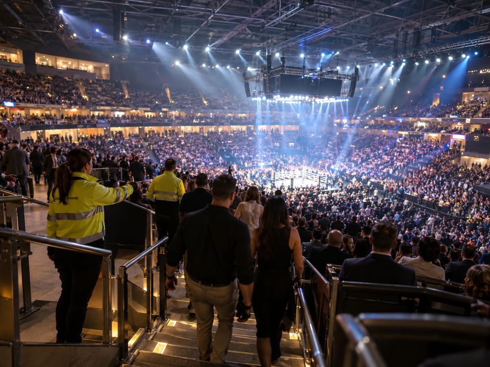 Event staff in high-visibility jackets guiding guests down the stairs of a packed indoor arena.